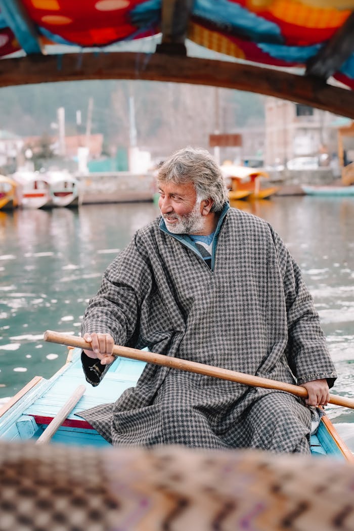 A man in traditional attire skillfully rows a wooden boat on a tranquil lake background.