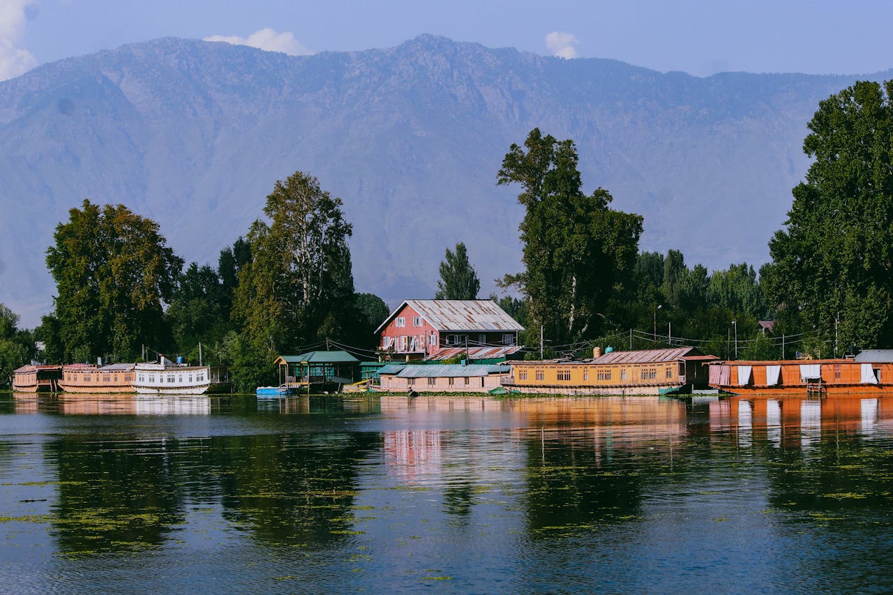 Scenic view of Dal Lake in Kashmir, showcasing houseboats and mountains under a clear sky.
